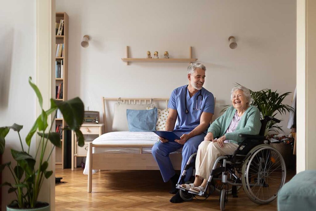 Older adult sits with a leashed dog in a bright assisted living common room.